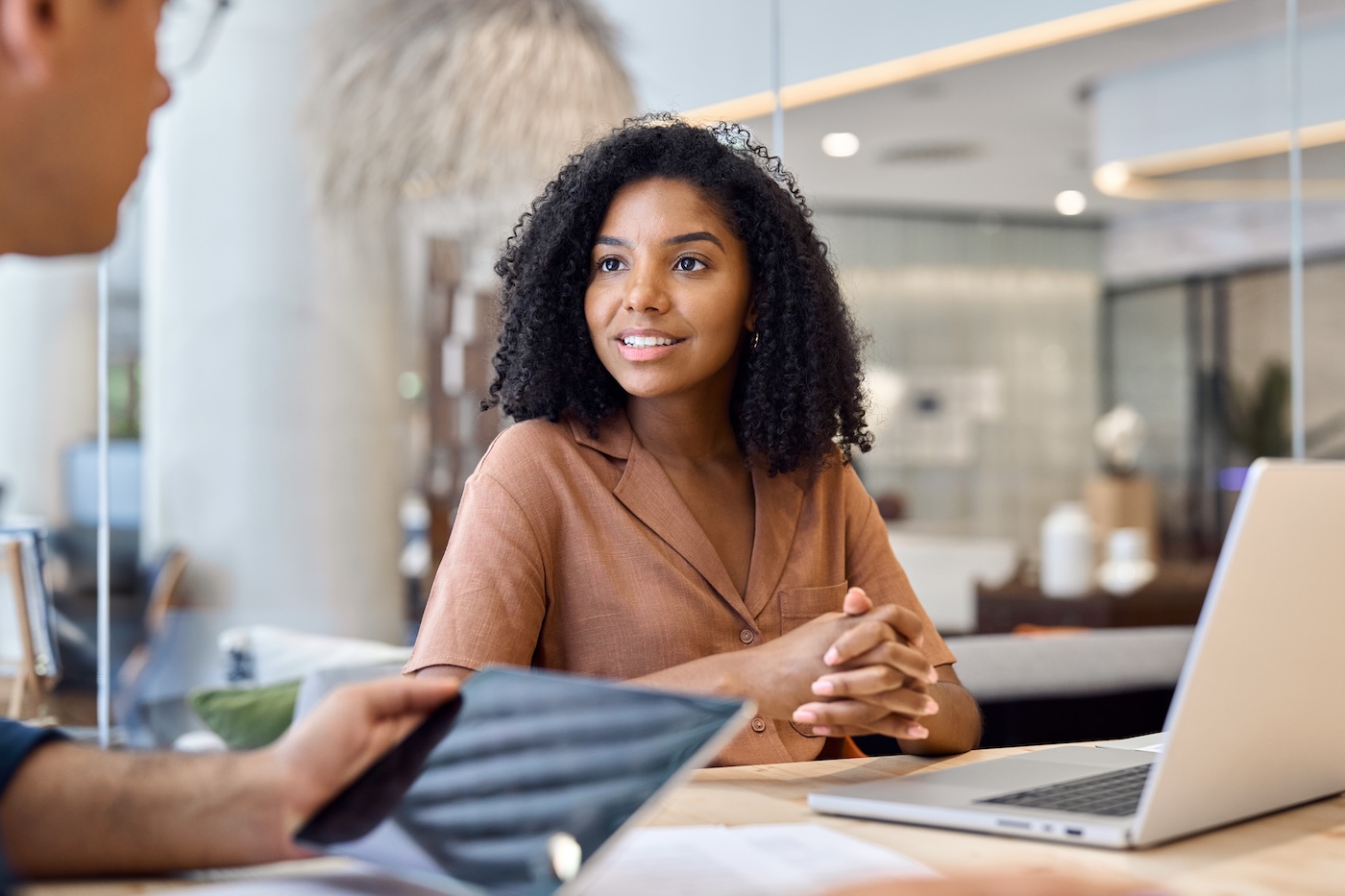 Young professional African American business woman manager talking to male colleague or consulting client at corporate meeting. Busy business team people working together using technology in office.